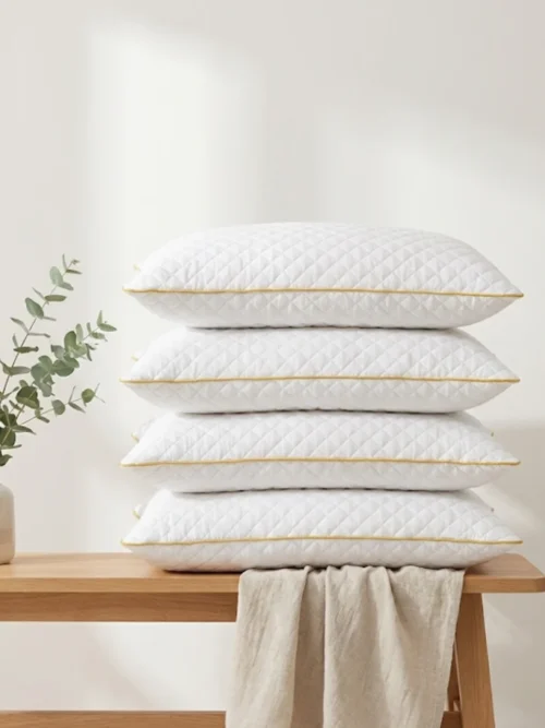 Stack of white quilted microfiber pillows with golden piping on wooden bench - premium bedroom decor